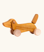Bajo Natural Dachshund Puppy in unpainted natural wood, a push-along toy for toddlers with floppy ears, an upright tail, and four wooden wheels, available online from Babipur.