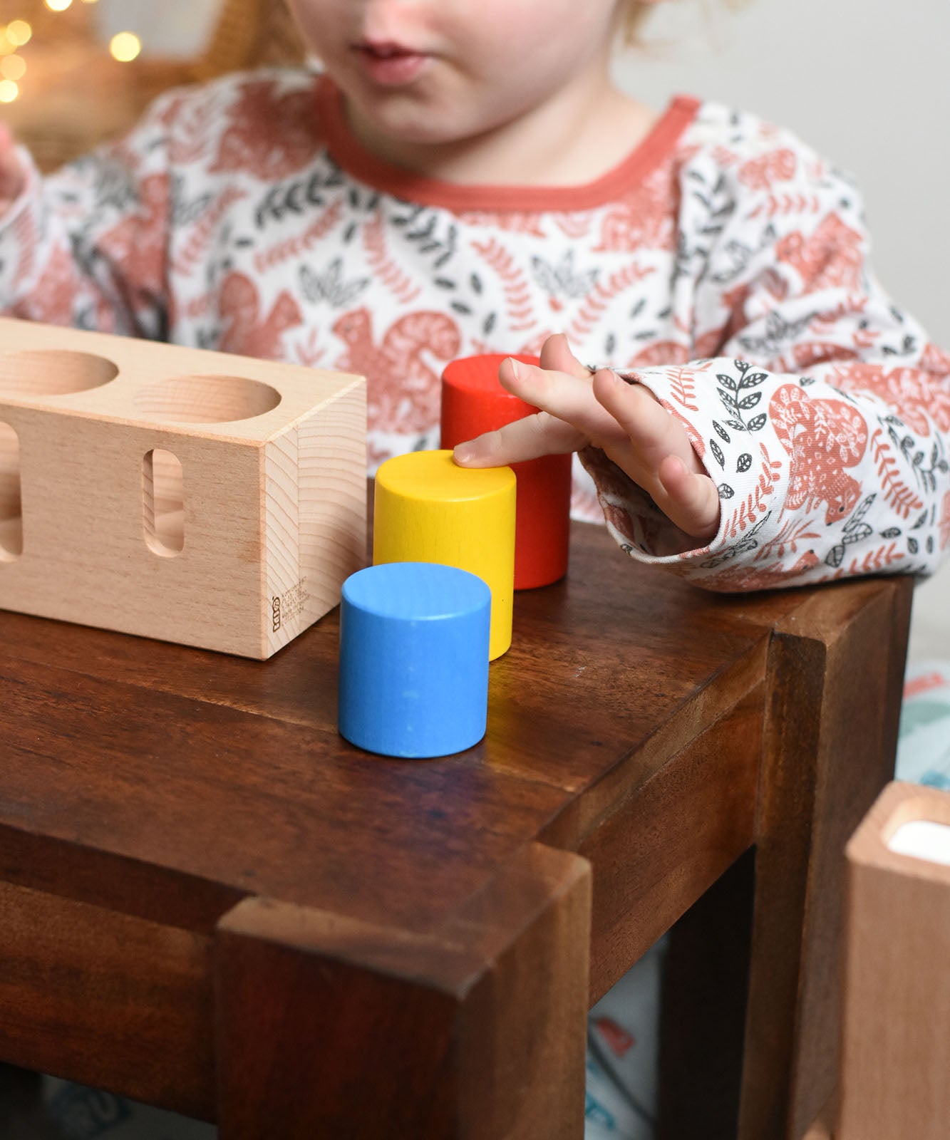 A child playing with the Bajo Deep And Shallow Sorter wooden toy placed on a small wooden table. All the cylinder shaped blocks have been placed besides the wooden base. These heirloom quality toys by Bajo are part of a wide range of wooden toys available here at Babipur.