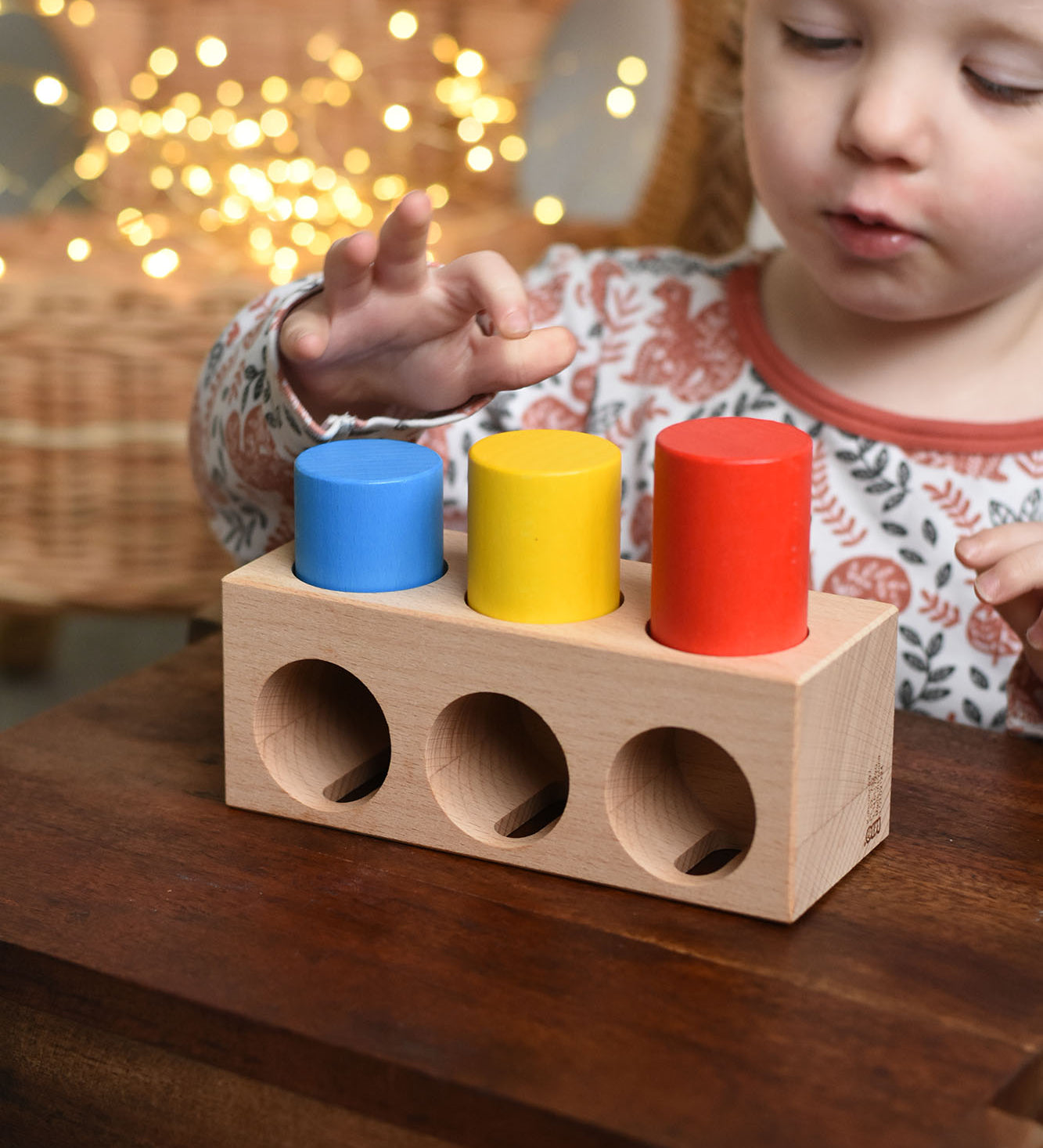 A child playing with the Bajo Deep And Shallow Sorter wooden toy placed on a small wooden table. These heirloom quality toys by Bajo are part of a wide range of wooden toys available here at Babipur. 