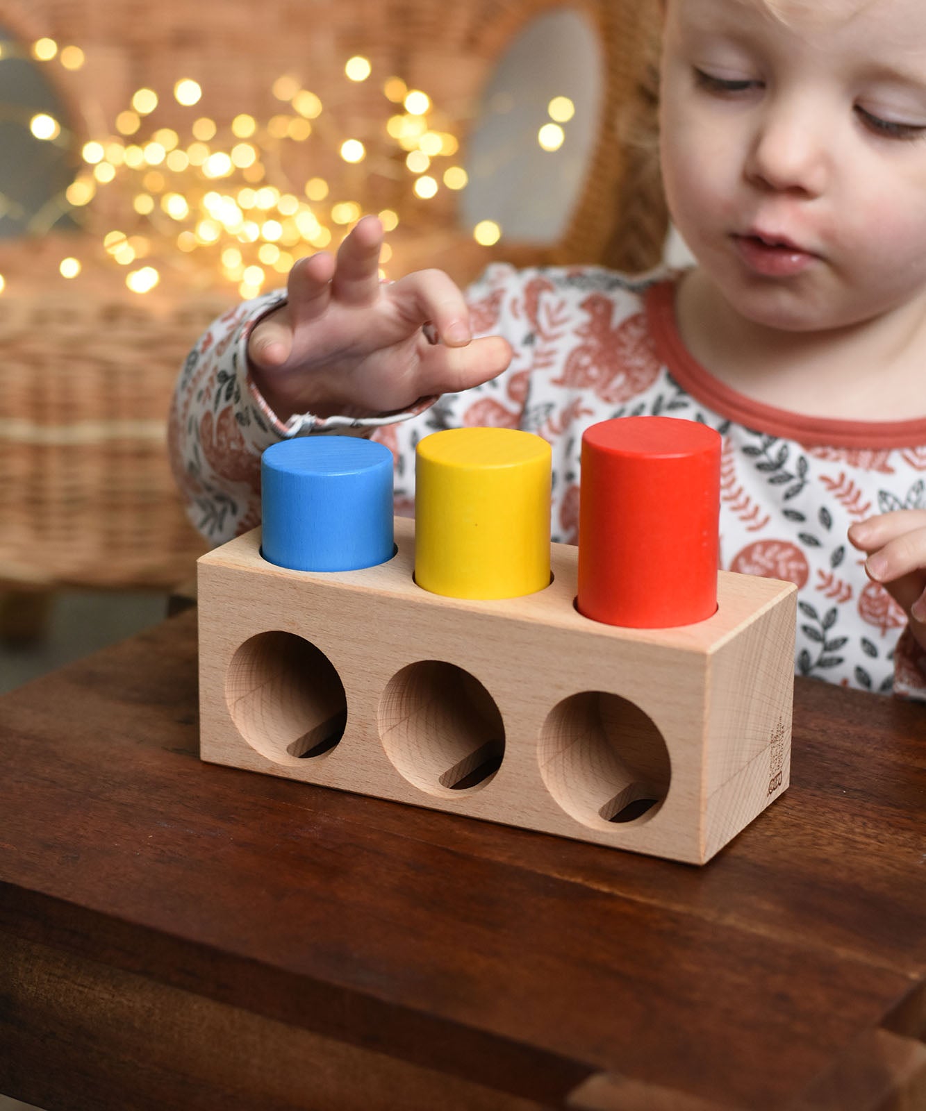 A child playing with the Bajo Deep And Shallow Sorter wooden toy placed on a small wooden table. These heirloom quality toys by Bajo are part of a wide range of wooden toys available here at Babipur. 