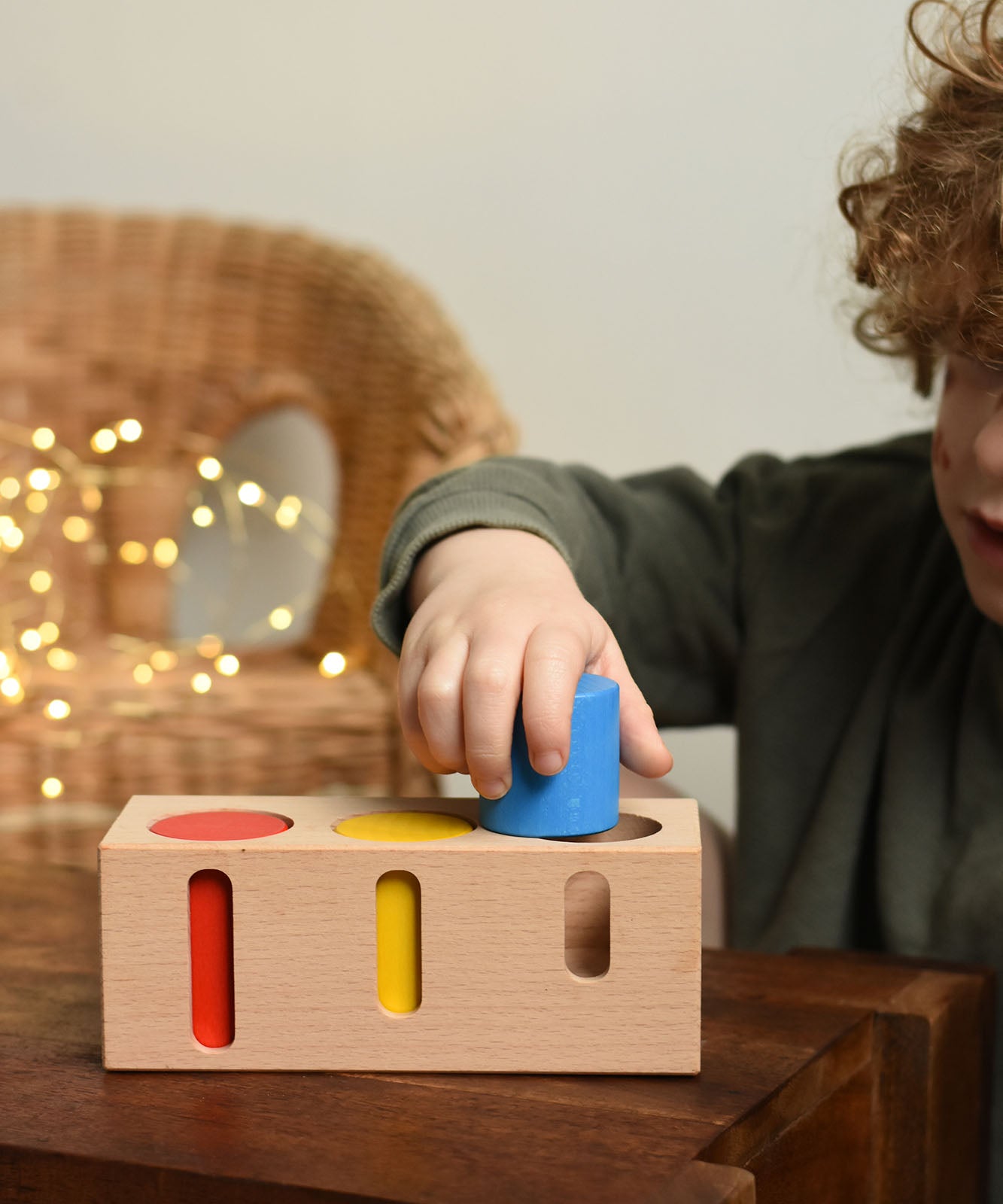 A child playing with the Bajo Deep And Shallow Sorter wooden toy placed on a small wooden table. These heirloom quality toys by Bajo are part of a wide range of wooden toys available here at Babipur. 