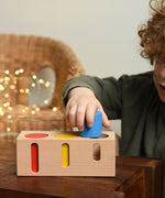 A child playing with the Bajo Deep And Shallow Sorter wooden toy placed on a small wooden table. These heirloom quality toys by Bajo are part of a wide range of wooden toys available here at Babipur. 