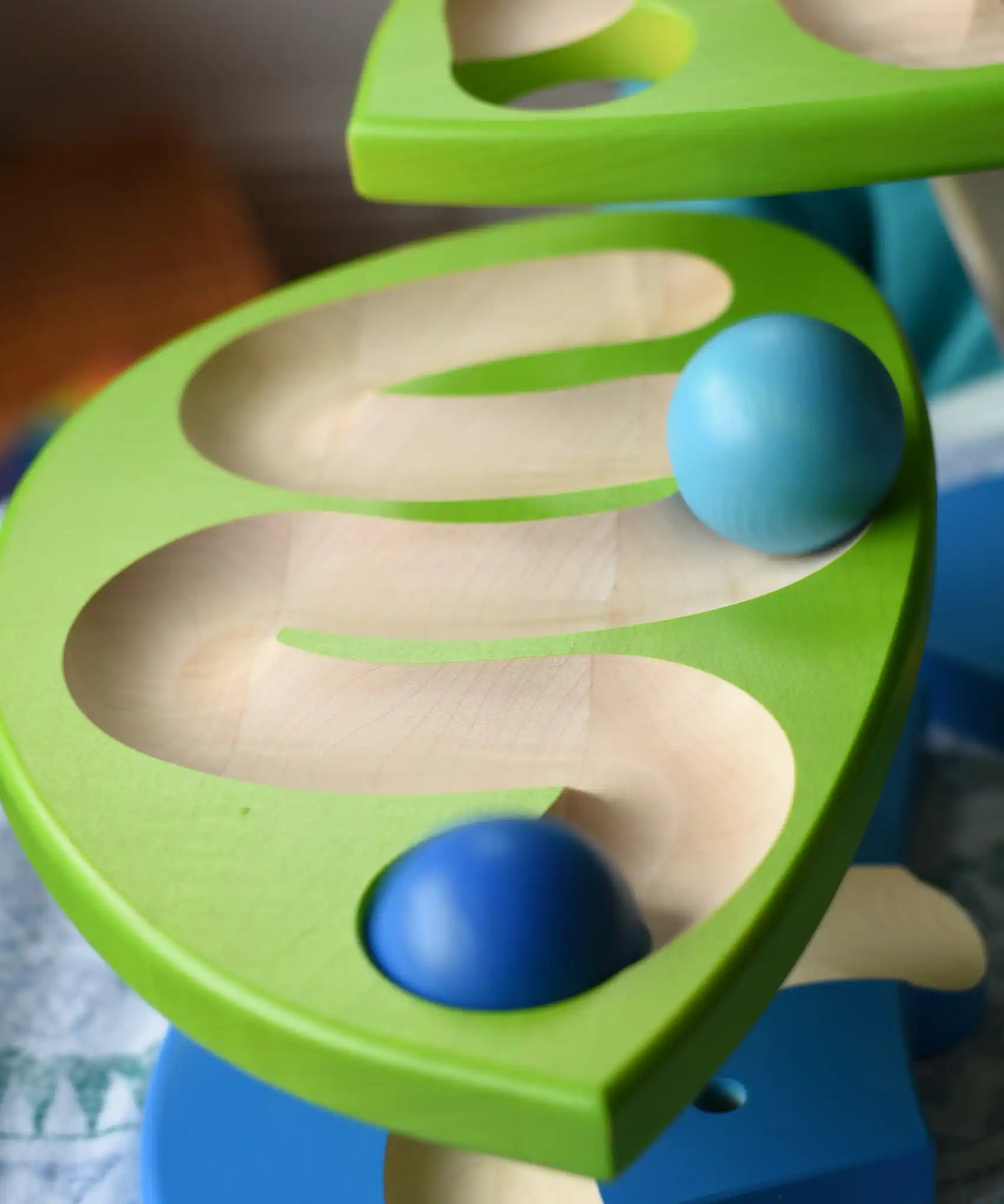 Close up of blue wooden balls rolling down one of the leaves on the Bajo Dewdrop, Coloured wooden ball run.