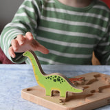 Bajo Wooden Dinosaur Puzzle with 6 colourful figures. Child's hand reaching for the green Brontosaurus figure. 