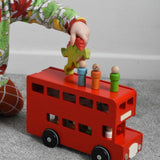 A child playing with the Bajo London bus wooden toy. The child has placed some of the wooden peg dolls on the roof of the bus and is walking a Holztiger Spinosaurus dinosaur wooden toy figure over the roof. These heirloom quality toys by Bajo are part of a wide range of wooden toys available here at Babipur