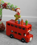 A child playing with the Bajo London bus wooden toy. The child has placed some of the wooden peg dolls on the roof of the bus and is walking a Holztiger Spinosaurus dinosaur wooden toy figure over the roof. These heirloom quality toys by Bajo are part of a wide range of wooden toys available here at Babipur