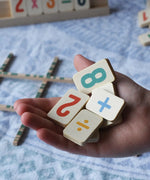 Wooden number and symbol tiles from the Bajo toys wooden easy maths learning set in an child's hand. 