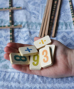 Wooden number and symbol tiles from the Bajo toys wooden easy maths learning set in an child's hand. 