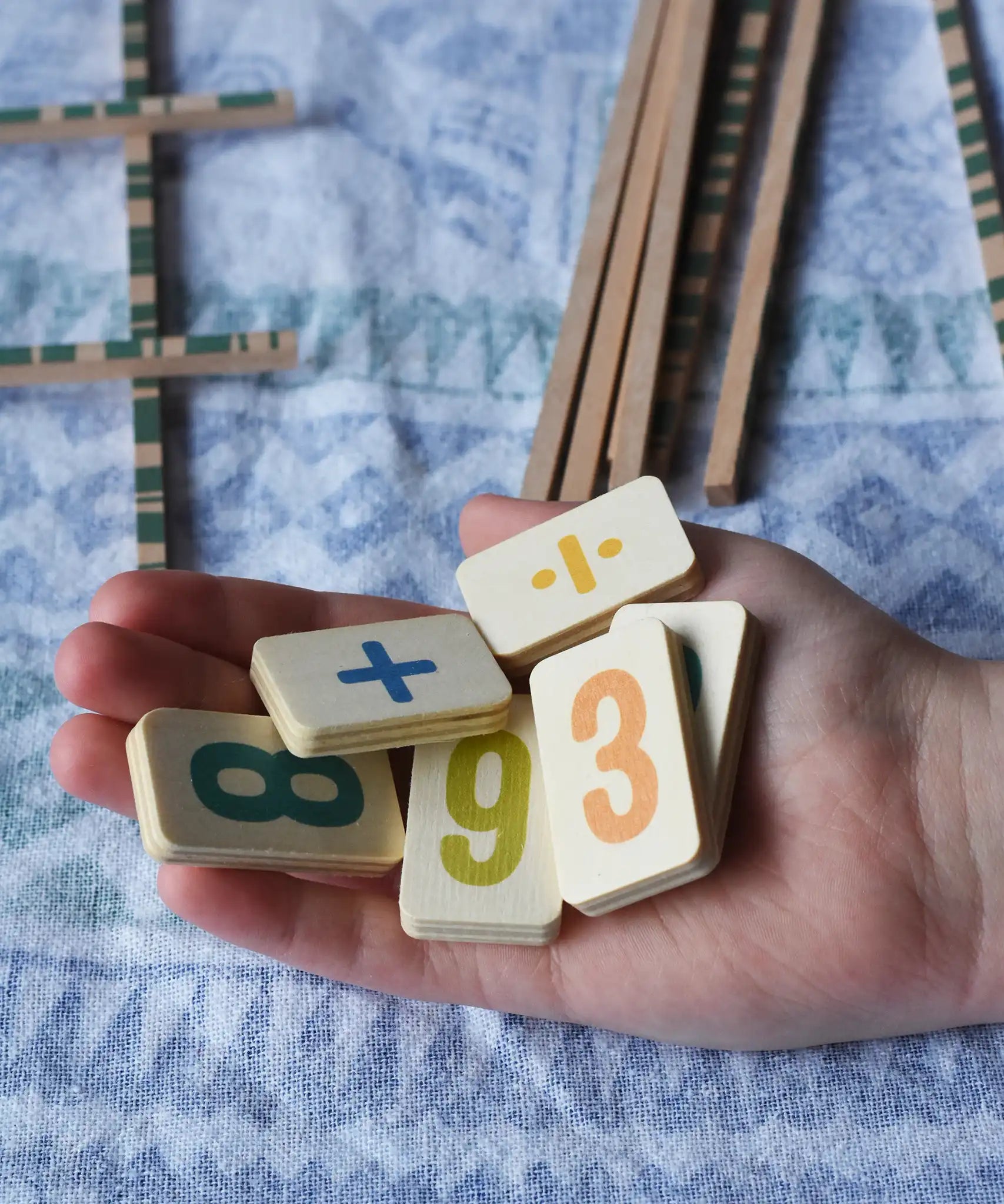 Wooden number and symbol tiles from the Bajo toys wooden easy maths learning set in an child's hand. 