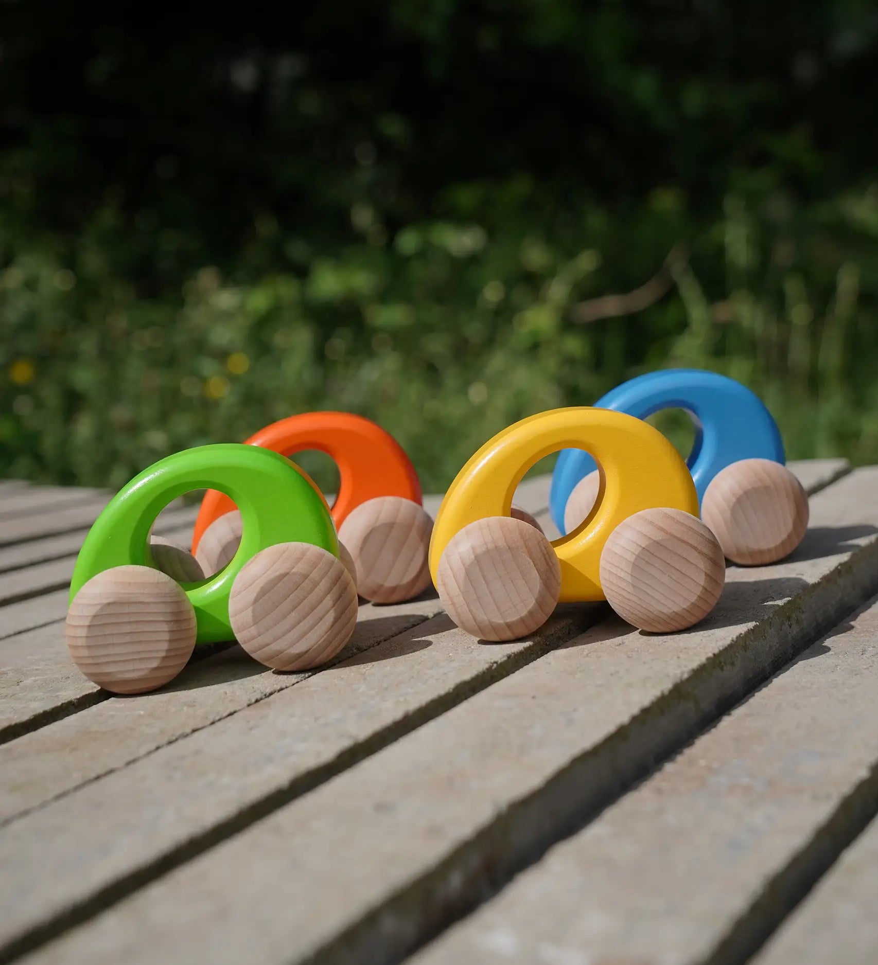 A group of Bajo handmade wooden ellipse toy cars standing on a concrete surface