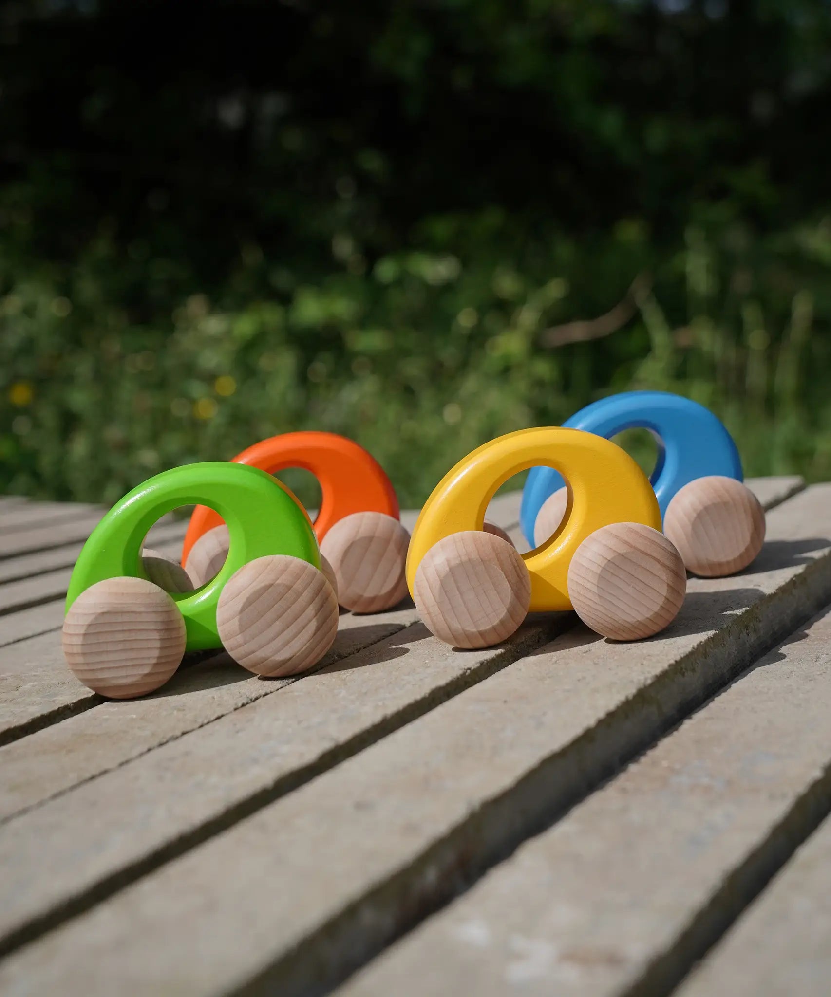 A group of Bajo handmade wooden ellipse toy cars standing on a concrete surface