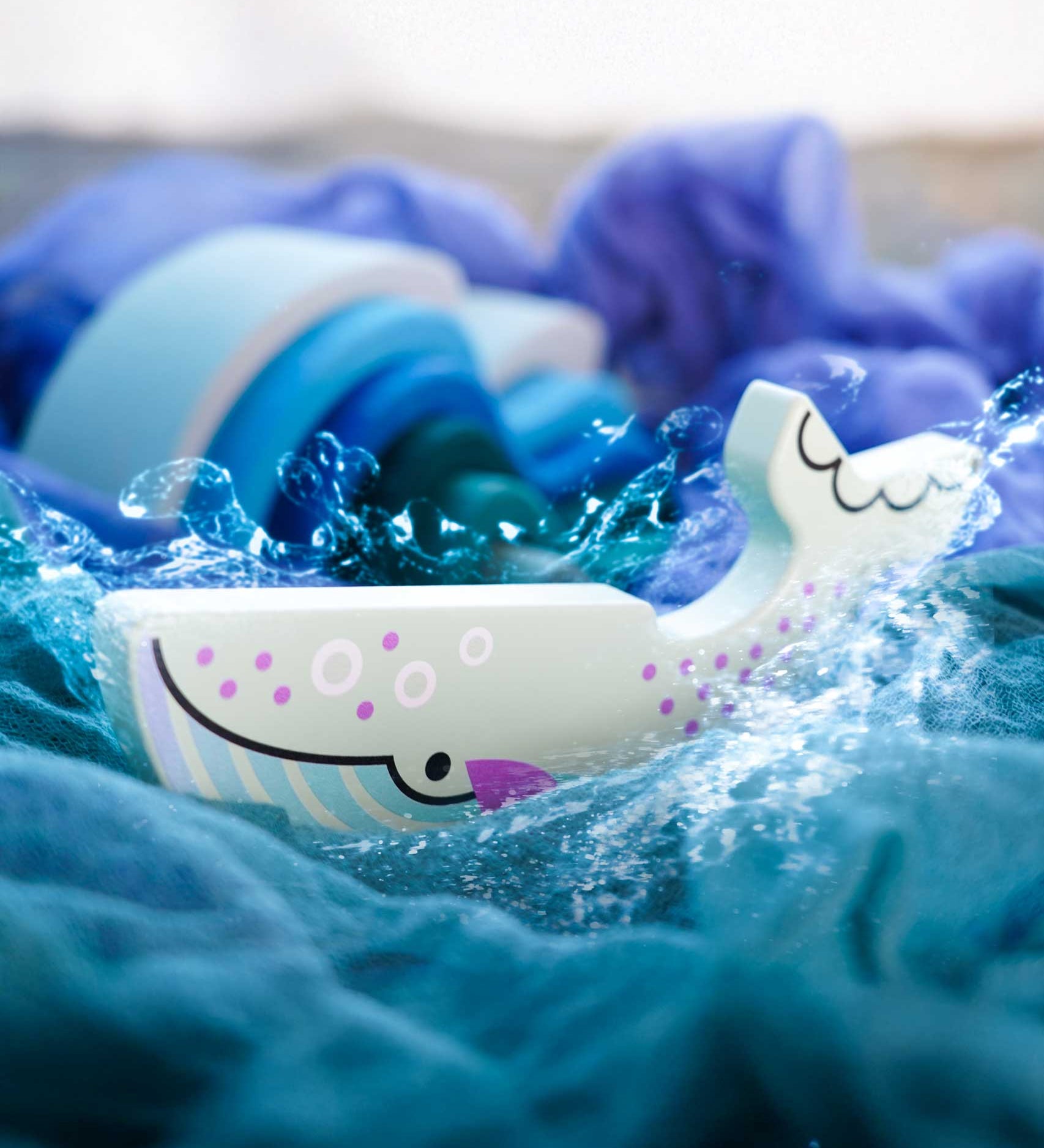 A Bajo Blue Whale Endangered Animals wooden toy Figure placed on Ostheimer cloths with Grimm's waves in the background in the Babipur playroom. These heirloom quality toys by Bajo are part of a wide range of wooden toys available here at Babipur.