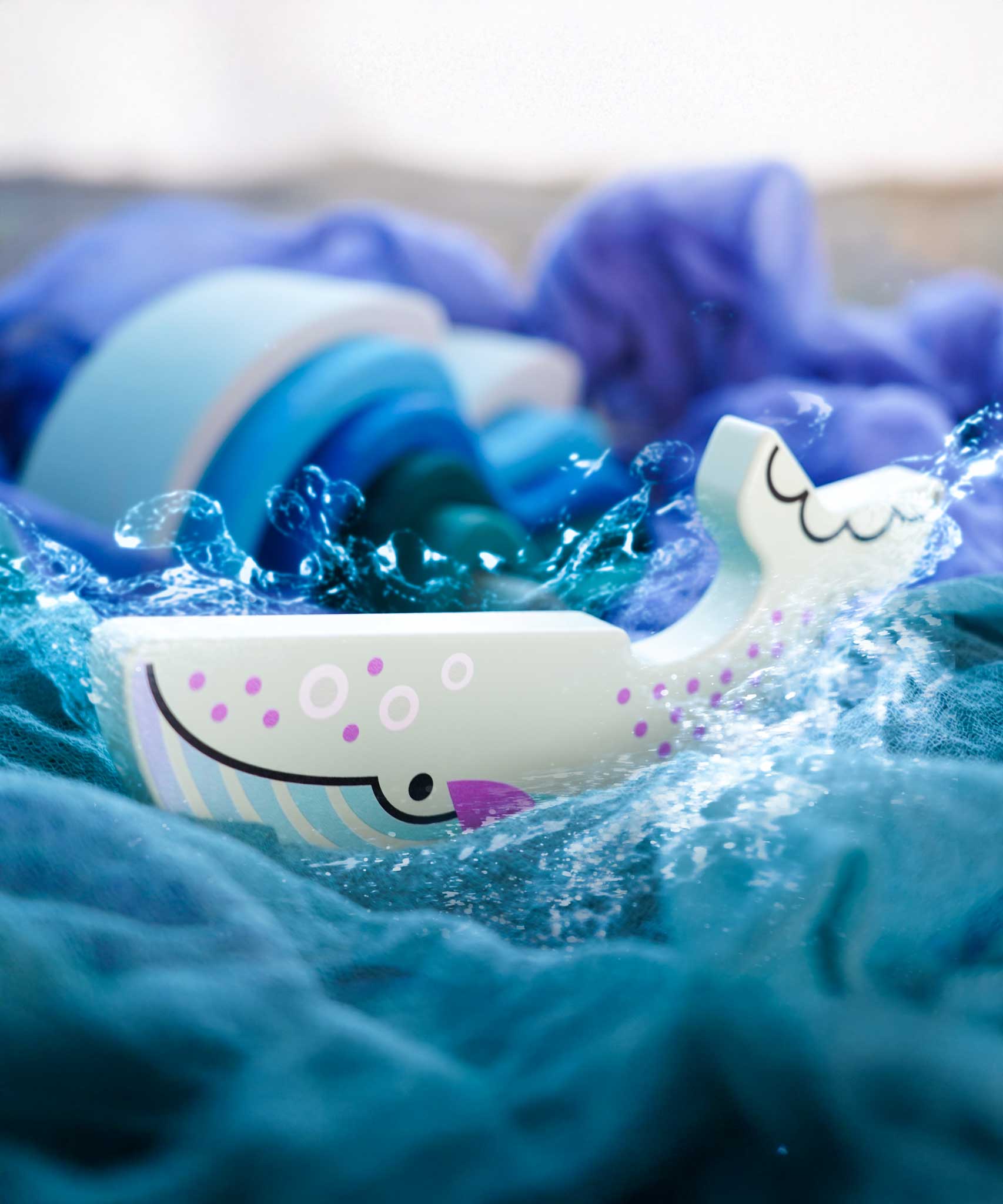 A Bajo Blue Whale Endangered Animals wooden toy Figure placed on Ostheimer cloths with Grimm's waves in the background in the Babipur playroom. These heirloom quality toys by Bajo are part of a wide range of wooden toys available here at Babipur.