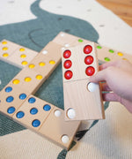 An adult's hand holding a domino from the Bajo gaint dominos set. These heirloom quality toys by Bajo are part of a wide range of wooden toys available here at Babipur. 