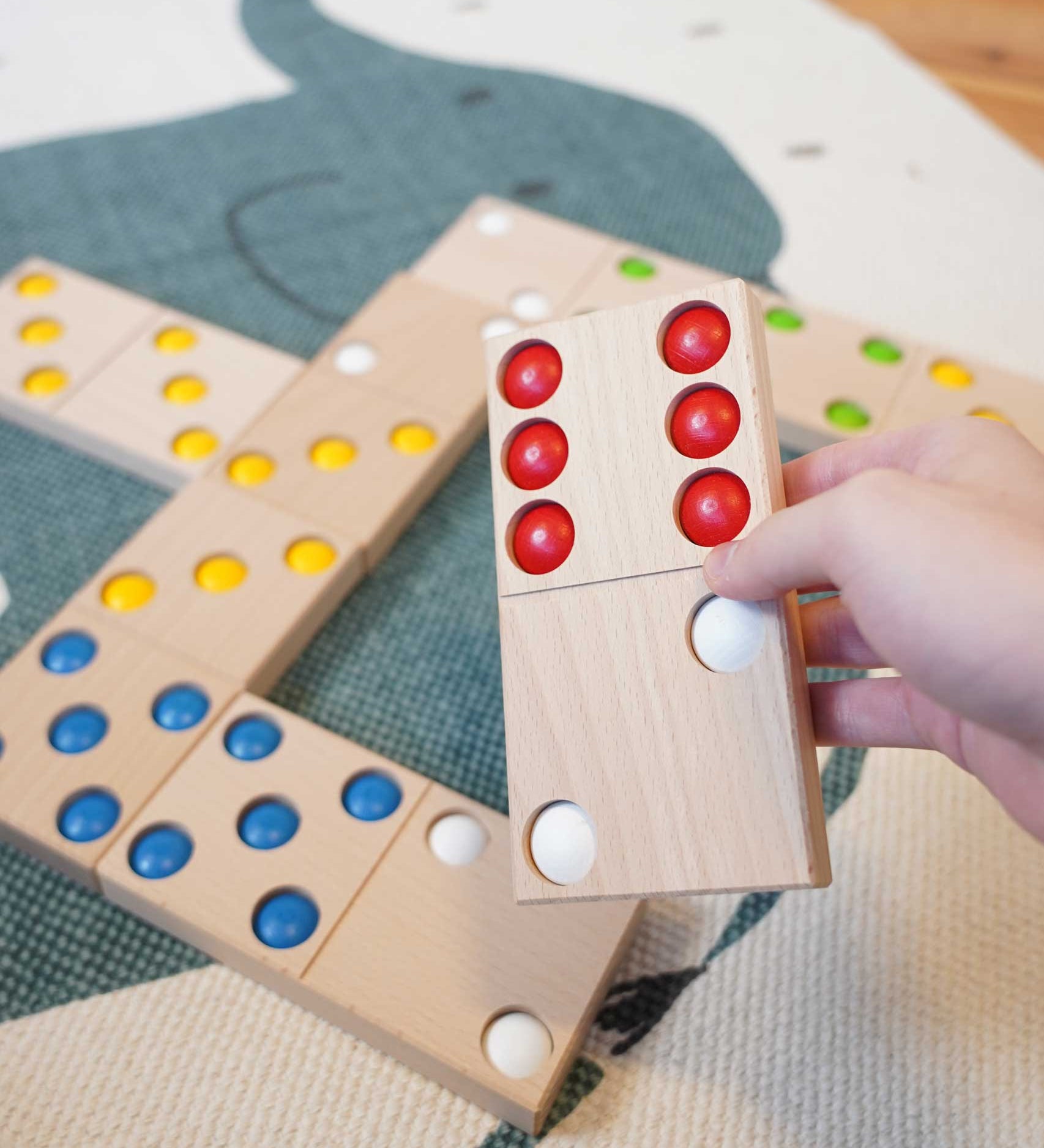 An adult's hand holding a domino from the Bajo gaint dominos set. These heirloom quality toys by Bajo are part of a wide range of wooden toys available here at Babipur. 