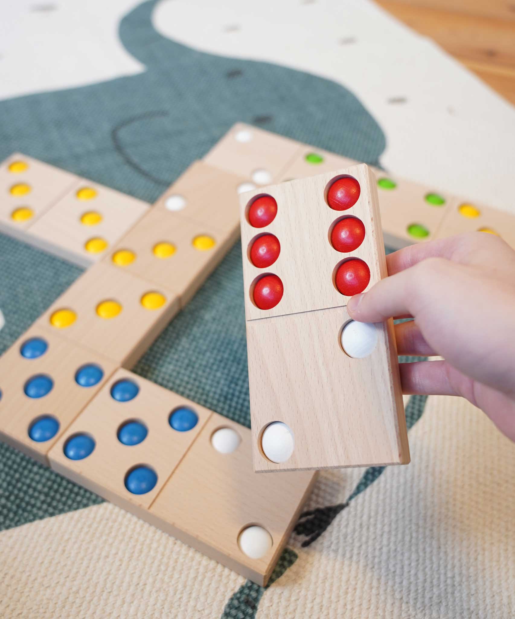 An adult's hand holding a domino from the Bajo gaint dominos set. These heirloom quality toys by Bajo are part of a wide range of wooden toys available here at Babipur. 