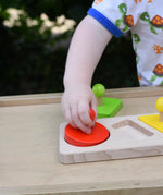 Child playing with the Bajo figures shapes sorting board, placing the red circle piece into the wooden base frame.