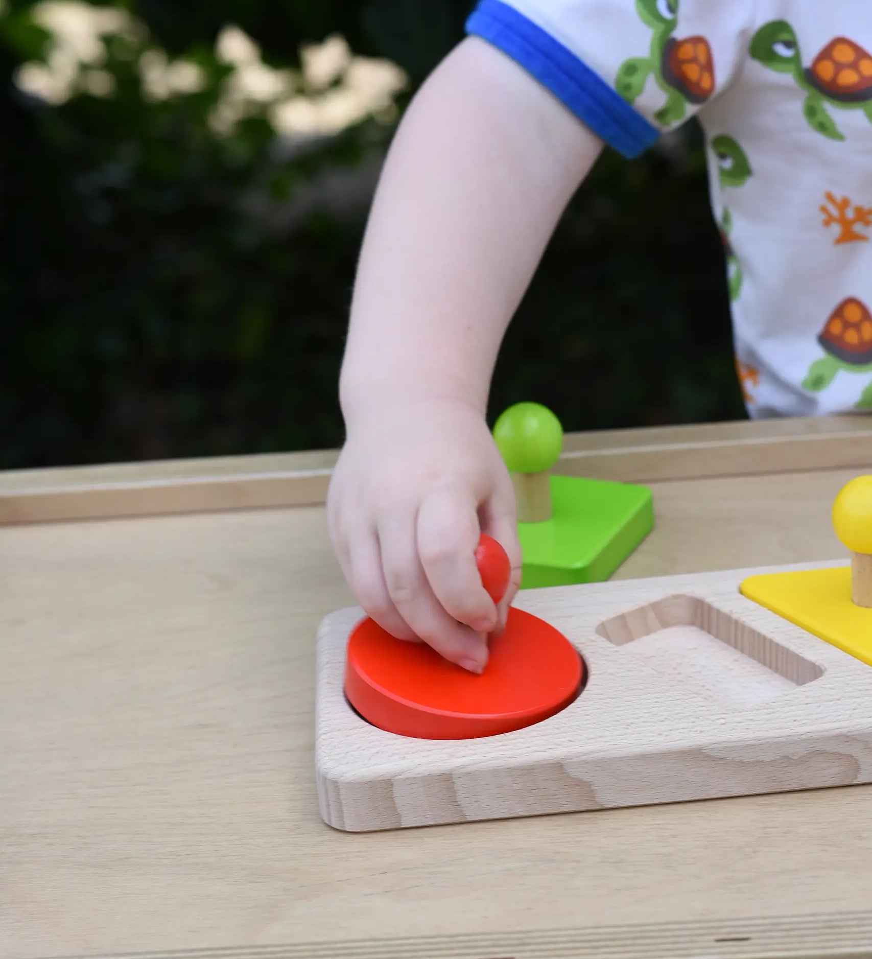 Child playing with the Bajo figures shapes sorting board, placing the red circle piece into the wooden base frame.
