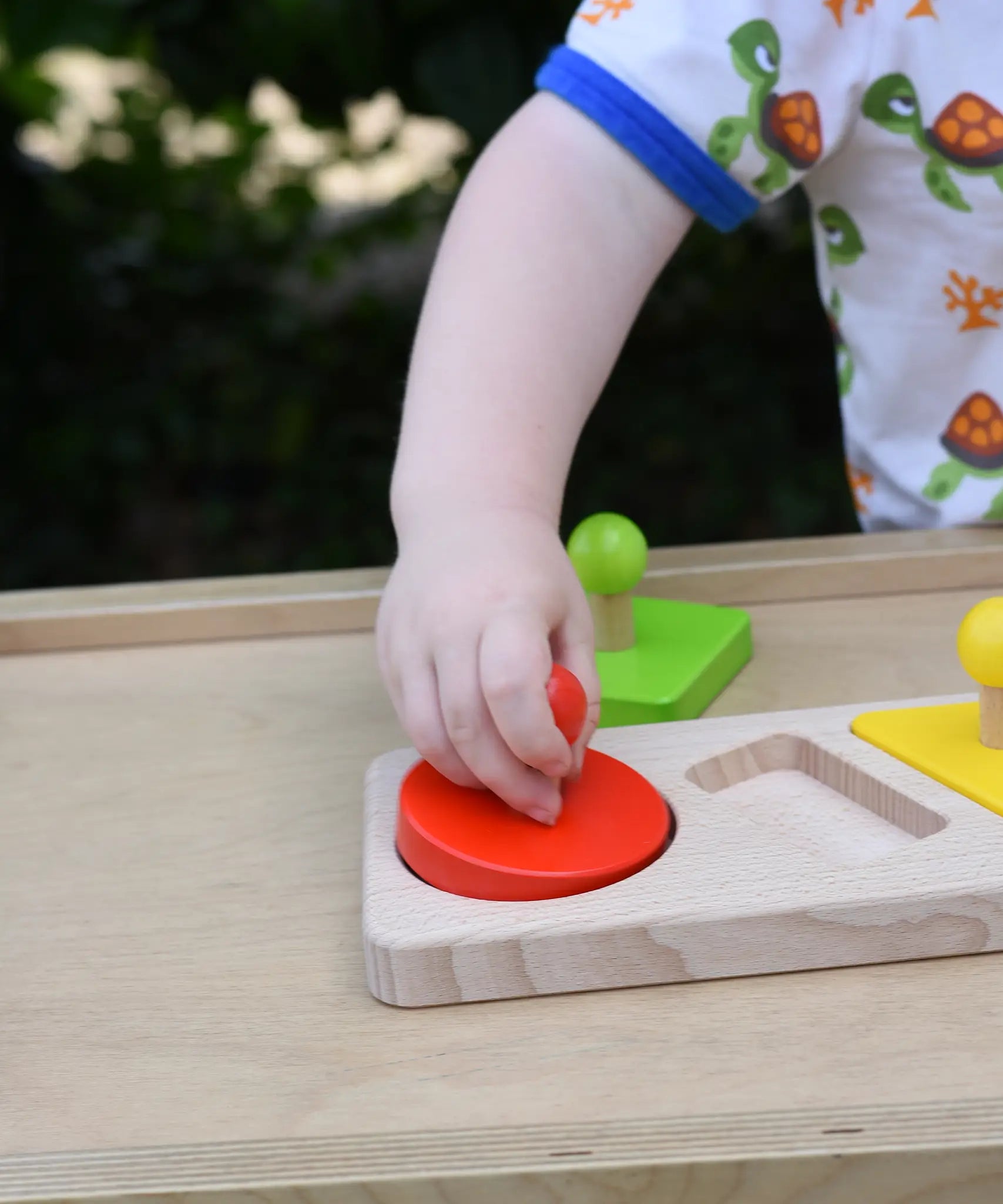 Child playing with the Bajo figures shapes sorting board, placing the red circle piece into the wooden base frame.