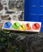 Bajo figures shapes sorting board placed on a stone wall outdoors.