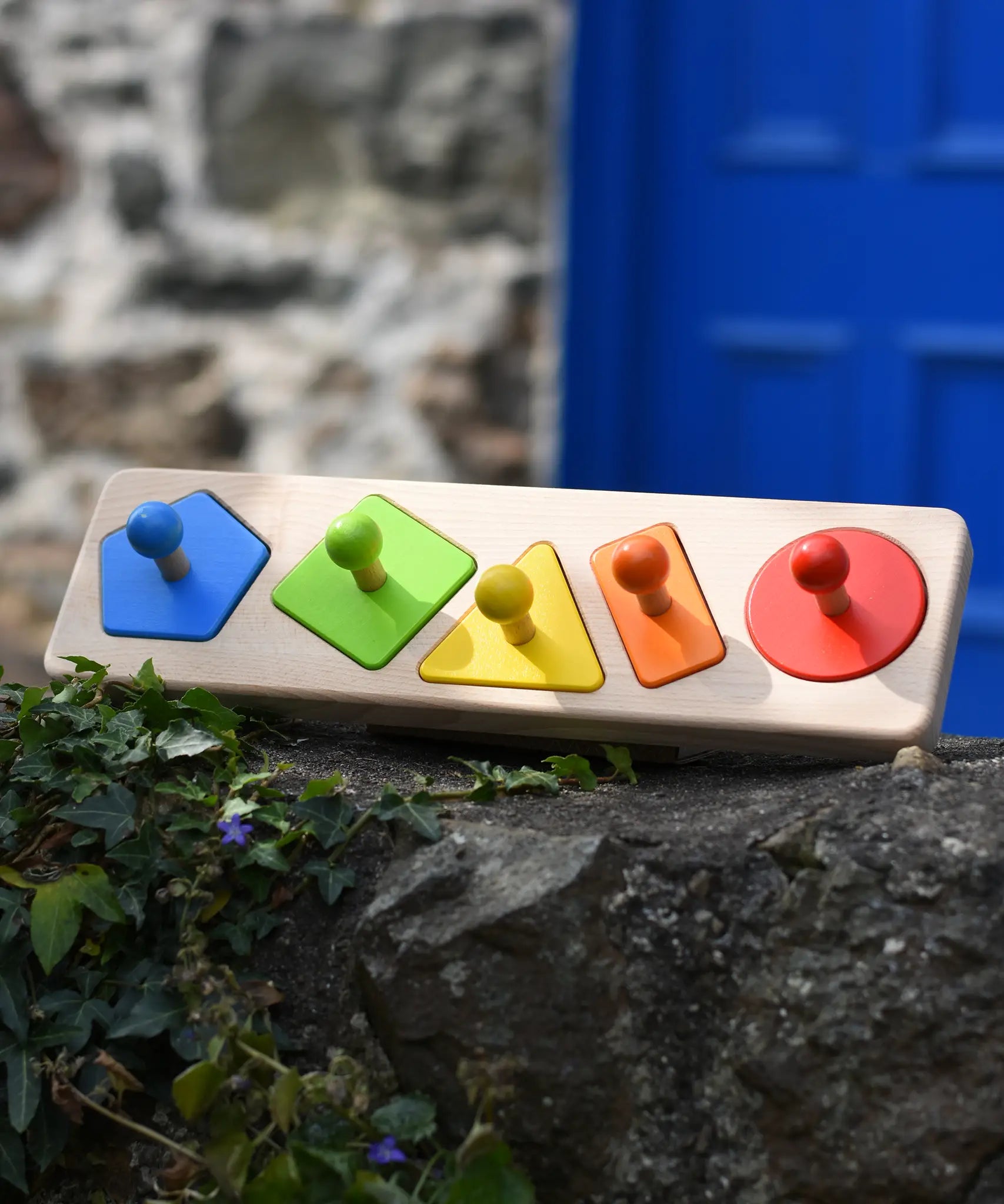 Bajo figures shapes sorting board placed on a stone wall outdoors.