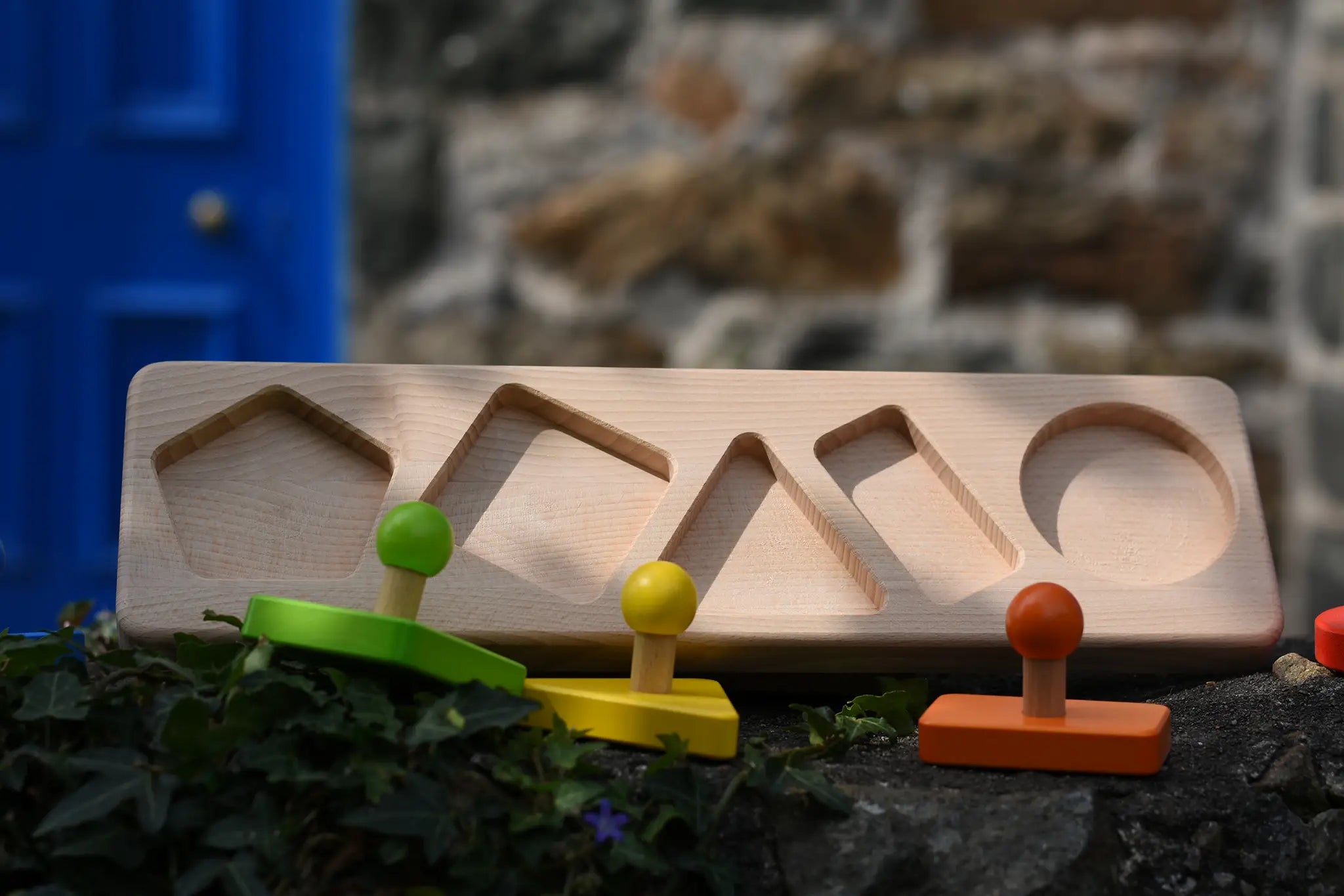 Bajo figures shapes sorting board base placed on a stone wall with the shapes taken out of the frame.