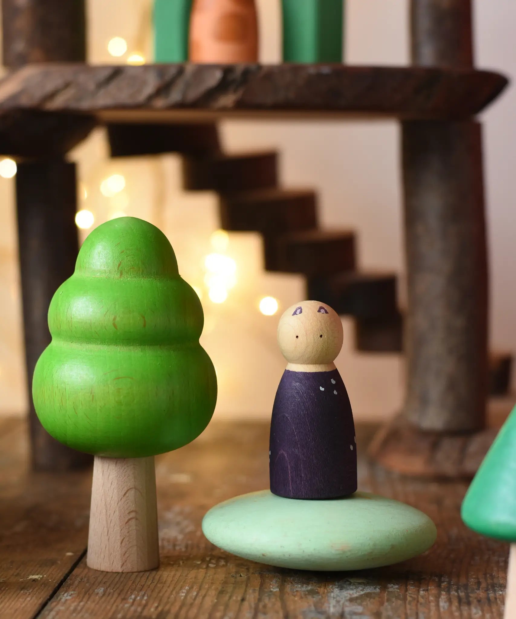 Large green bobble tree from the Bajo forest wooden toy tree figure set placed next to a Grapat animal Nin on a green Bajo pebble in a small world play scene.