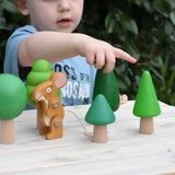 Child playing with the Bajo green forest tree set - 5 wooden trees in a set of 5 placed on a wooden surface with the Gruffalo mouse character figure. 
