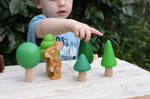 Child playing with the Bajo green forest tree set - 5 wooden trees in a set of 5 placed on a wooden surface with the Gruffalo mouse character figure. 
