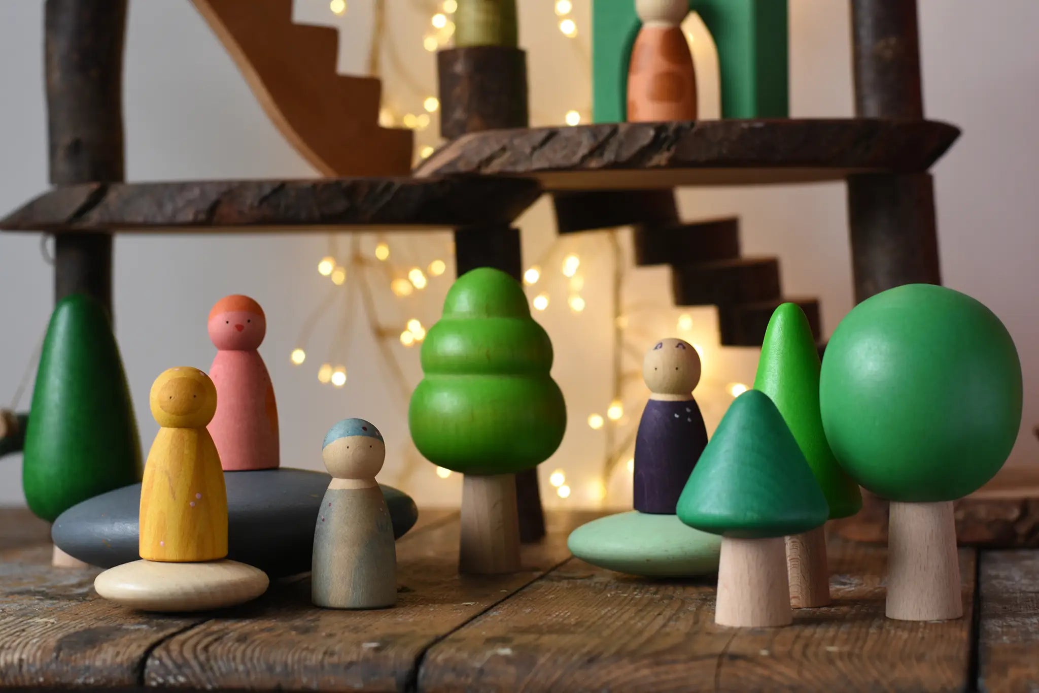 Bajo green forest tree set - 5 wooden trees in a set of 5 placed on a wooden surface amongst Bajo pebbles with Grapat animal crew Nins with a Magic Wood adventure playground in the background.
