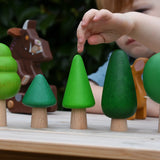 Child playing with the Bajo green forest tree set lining them up on a table. Gruffalo figure in the background.