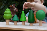 Child playing with the Bajo green forest tree set lining them up on a table. Gruffalo figure in the background.