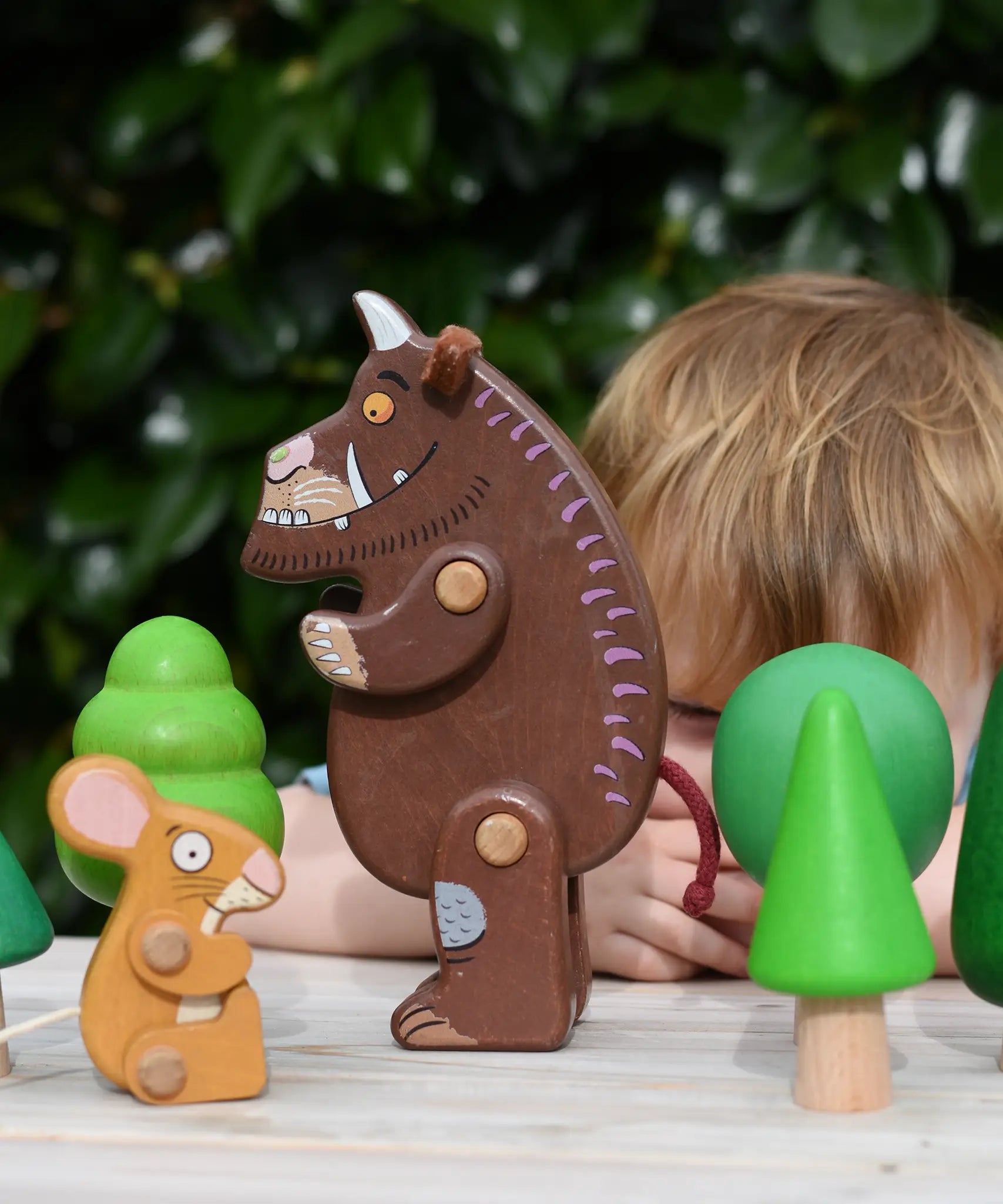 Child playing with the Bajo green forest tree set and the Gruffalo and mouse character figures. 
