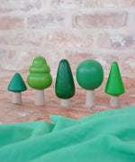 Bajo forest wooden toy tree figure set. Five green trees in different heights and shapes. Green laura's play cloth can be seen in the foreground.