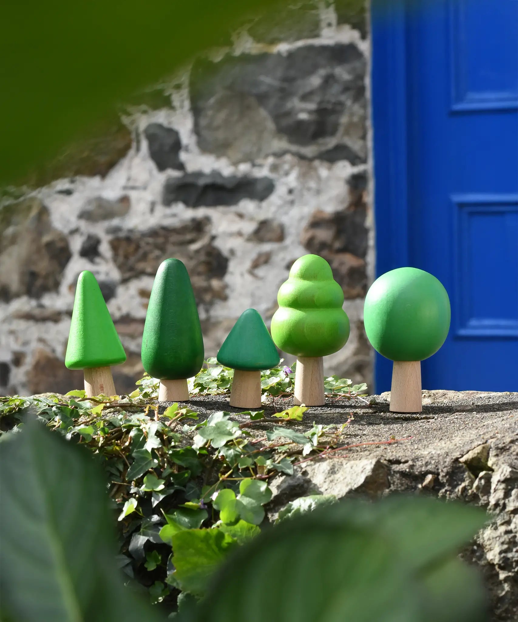 Bajo green forest tree set of wooden toy figures placed on a stone wall outdoors.