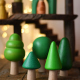 Bajo green forest tree set - 5 wooden trees in a set of 5 placed on a wooden surface with a Magic Wood adventure playground in the background.
