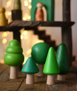 Bajo green forest tree set - 5 wooden trees in a set of 5 placed on a wooden surface with a Magic Wood adventure playground in the background.
