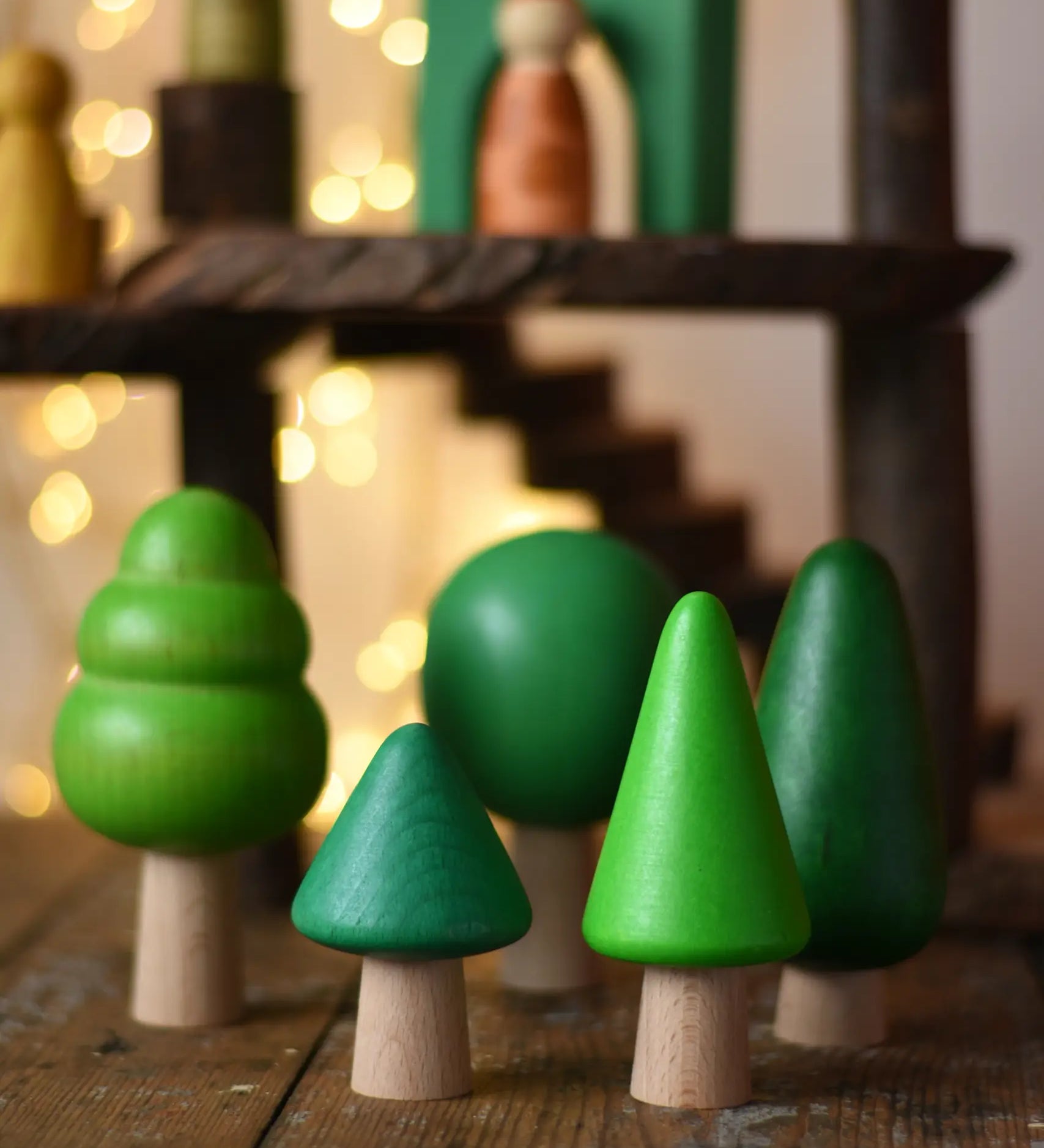 Bajo green forest tree set - 5 wooden trees in a set of 5 placed on a wooden surface with a Magic Wood adventure playground in the background.
