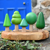 Bajo green forest tree set of 5 figures placed on a wooden dish placed on a stone wall outdoors.