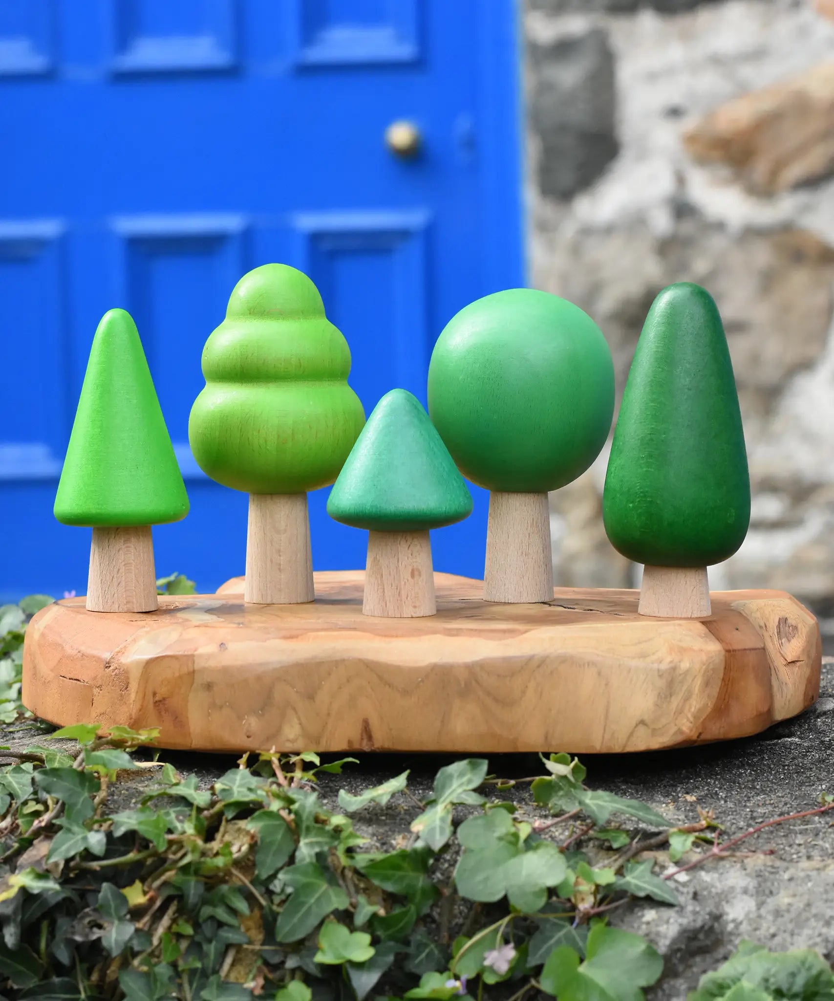 Bajo green forest tree set of 5 figures placed on a wooden dish placed on a stone wall outdoors.