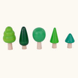 Bajo forest wooden toy tree figure set lined up. Five green trees in different heights and shapes. Green laura's play cloth can be seen in the foreground.