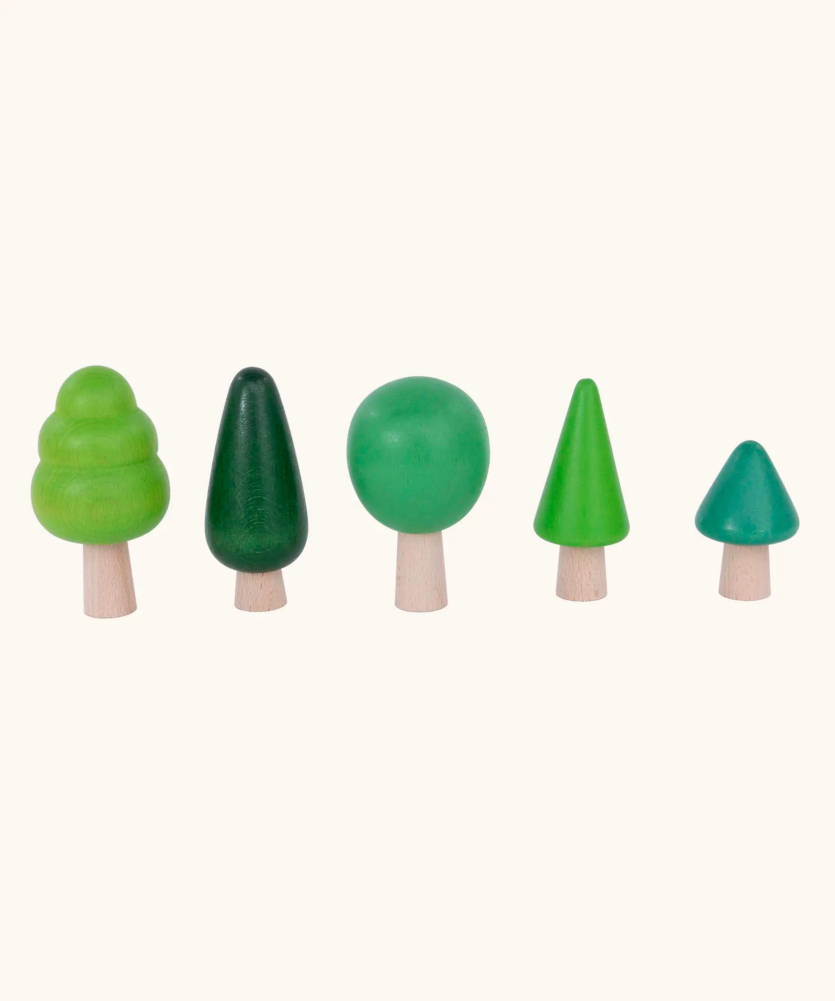 Bajo forest wooden toy tree figure set lined up. Five green trees in different heights and shapes. Green laura's play cloth can be seen in the foreground.
