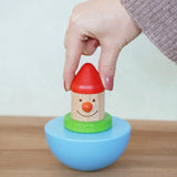 Adult's hand holding the Bajo roly poly wobbling dwarf wooden baby toy upright. Blue half sphere base that wobbles when pushed with a wooden dwarf character on top from Babipur