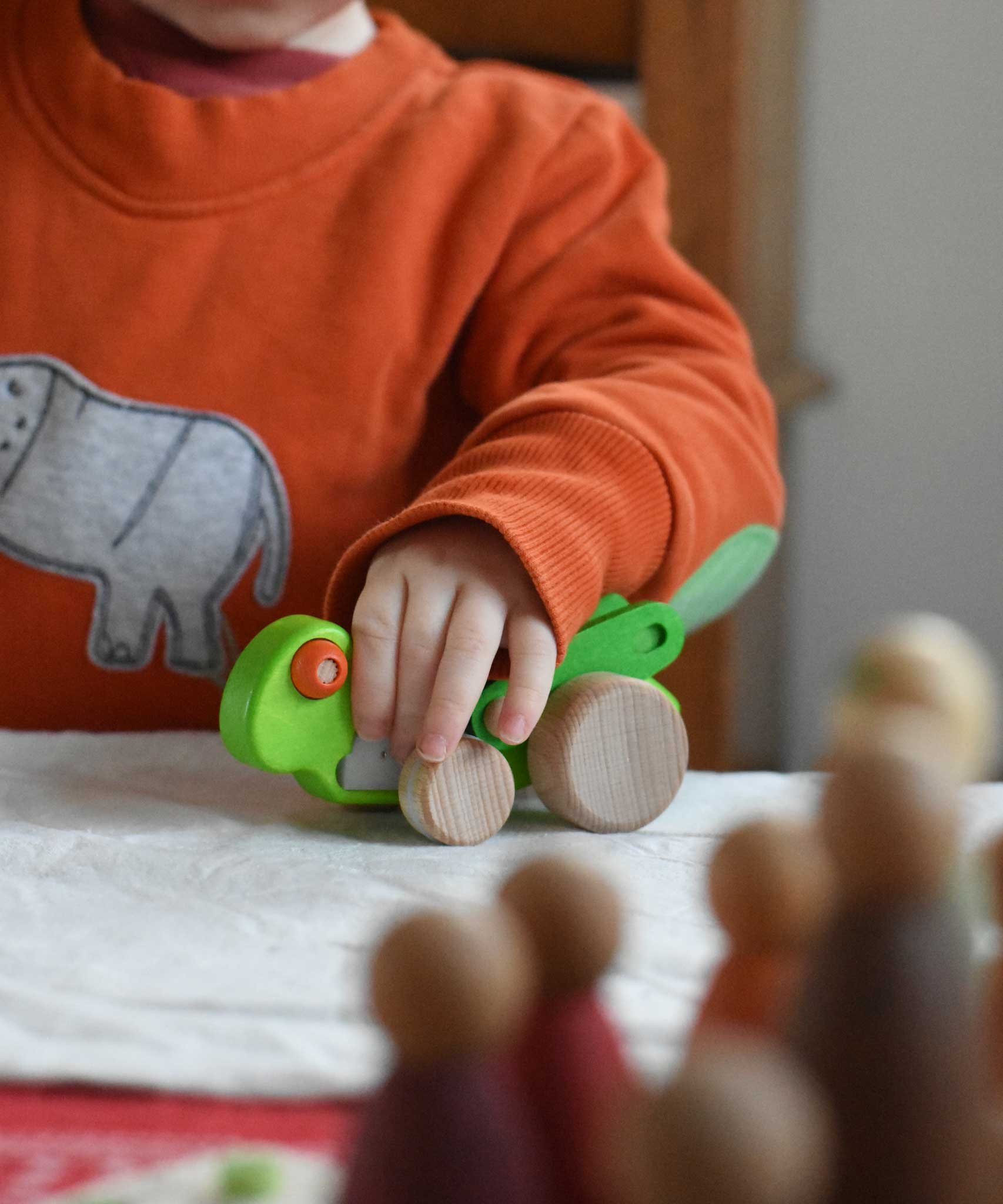 A child playing with the Bajo green Grasshopper wooden toy. These heirloom quality toys by Bajo are part of a wide range of wooden toys available here at Babipur.