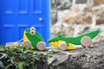 Bajo pull along crocodile and double frog wooden toys placed on a stone wall outdoors. 