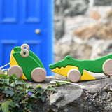 Bajo pull along crocodile and double frog wooden toys placed on a stone wall outdoors. 