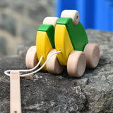 Bajo green double frogs pull along wooden toy placed on a stone wall. 