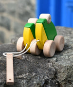 Bajo green double frogs pull along wooden toy placed on a stone wall. 