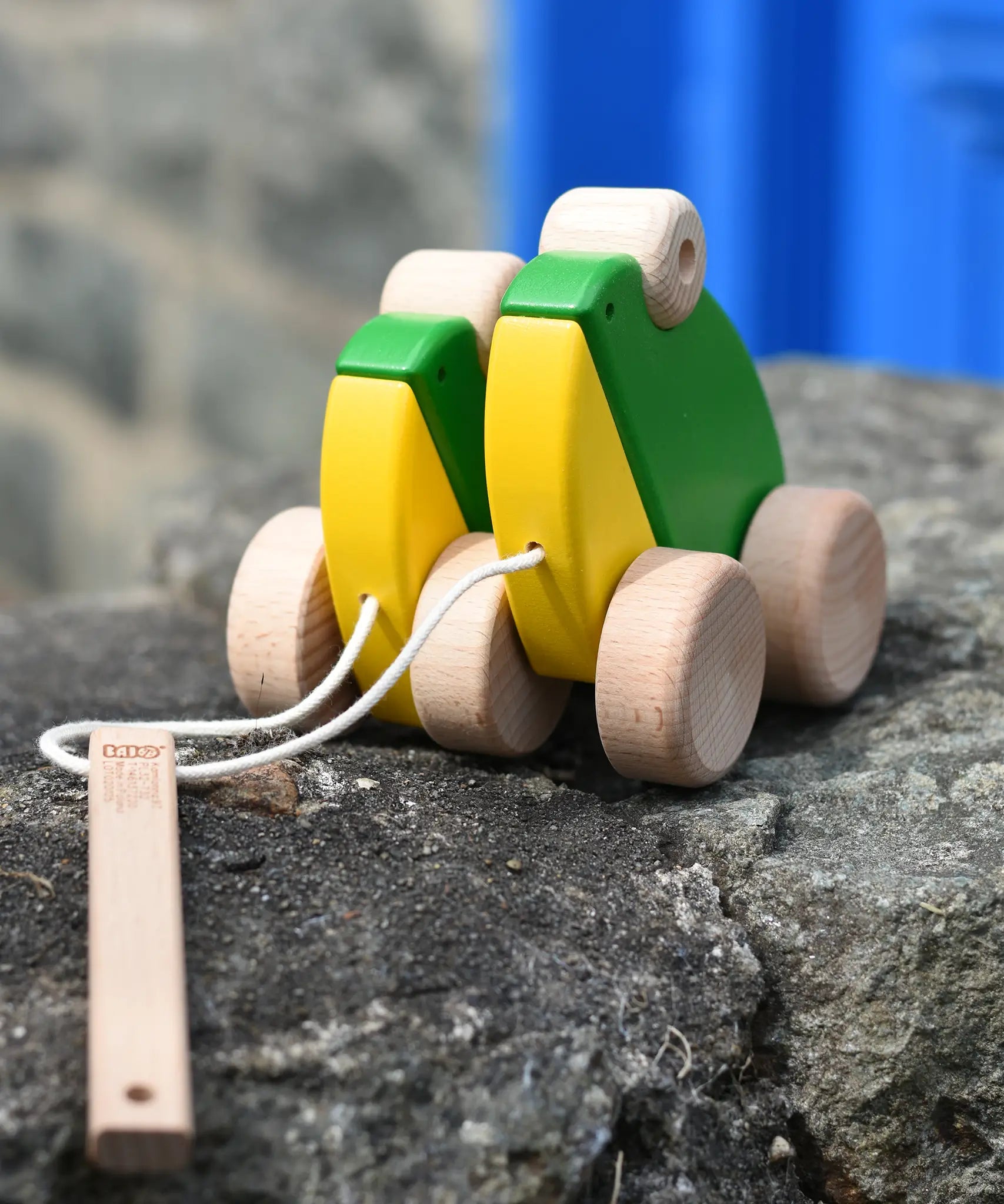 Bajo green double frogs pull along wooden toy placed on a stone wall. 