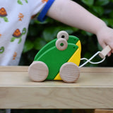 Child playing with the Bajo green double frogs pull along wooden toy, pulling it along the Miri slide.